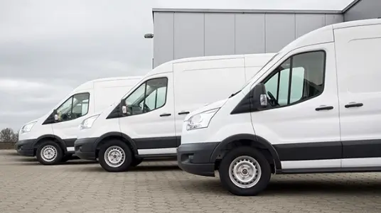 Three commercial white vans parked in a neat line, representing the availability of financing options for commercial vehicle fleets.